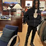 Polo G Spotted Shopping In A Prada Cropped Technical Knit Black Puffer Jacket, Polarius 19 Black Sneakers And Amiri Bones Applique Black Jeans
