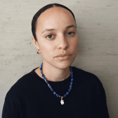 Portrait of a young person with a neutral expression and beaded necklace.